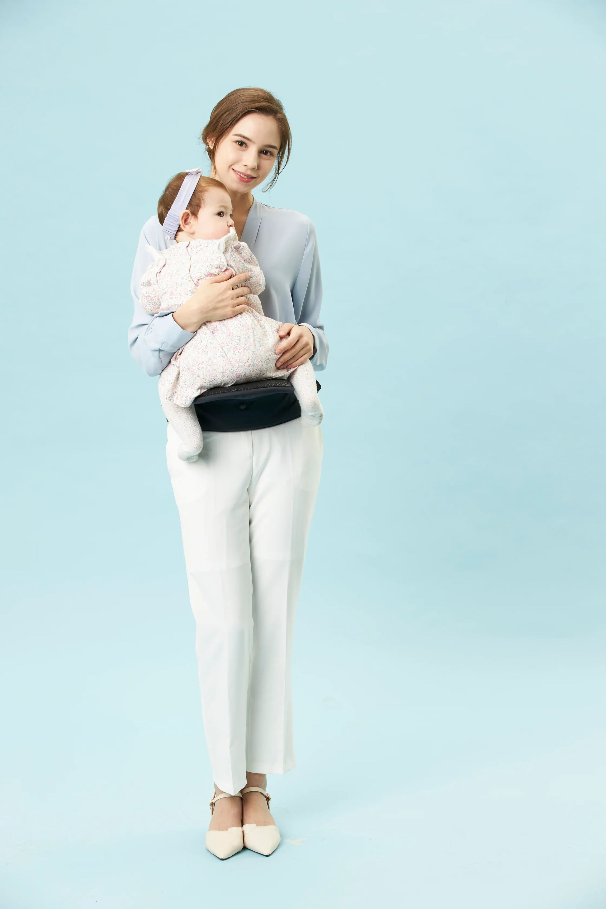 Mother using ergonomic baby carrier hip seat with baby, light blue background, bebefit.eu